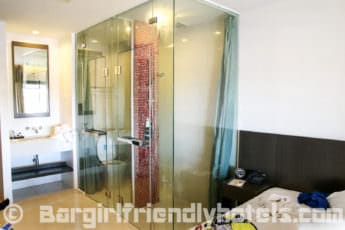 Glass enclosed shower next to the bed in Deluxe rooms of D Varee Diva Avenue Samui
